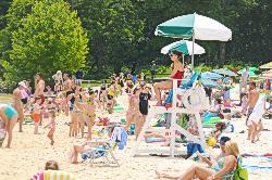 The beach filled during a summer festival weekend, with a guard posted under an umbrella courtesy of Virginia State Parks&nearr; (CC BY 2.0&nearr;)