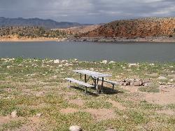A shoreline picnic table and fire ring at Gunlock State Park with the reservoir behind it courtesy of Thure Johnson&nearr; (CC BY 2.0&nearr;)