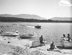 Swimmers and boats on a Seeley Lake beach in 1961, in a Lolo National Forest photo, with water skier courtesy of Forest Service Northern Region from Missoula, MT, USA&nearr; (Public domain&nearr;)