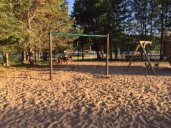 Swings and picnic tables on the sand by the water at the beach playground.