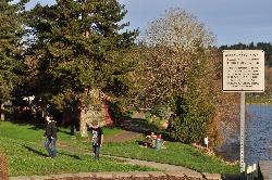The paved path and lawn at Horseshoe Lake Park, with the posted park hours sign and the lake on the  courtesy of Joe Mabel&nearr; (CC BY 3.0&nearr;)